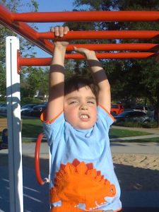 young boy child using monkey bars for motor planning& postural control
